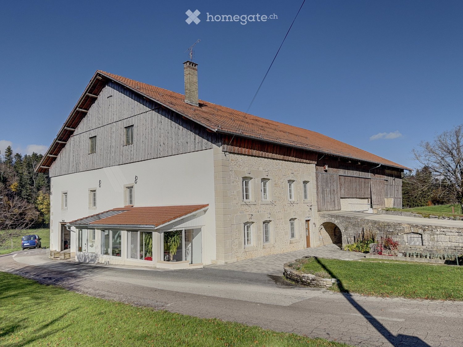 Large house with red roof, white walls, multiple windows, chimney, attached garage, driveway, garden, and a car parked in front.