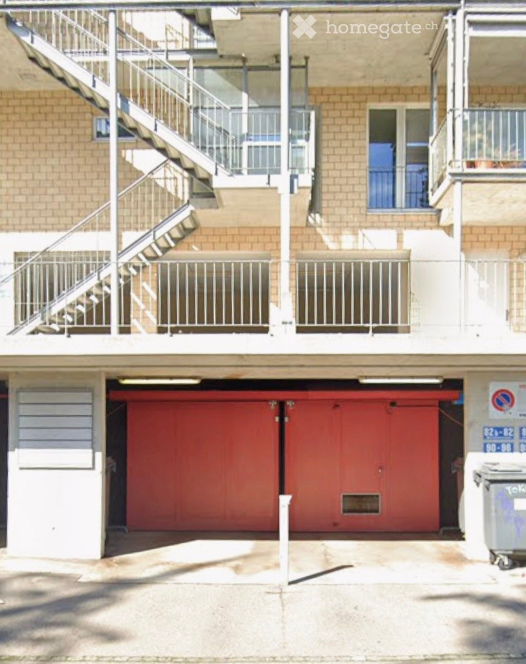 Apartment building with a garage entrance, brick walls, metal railings, and a staircase