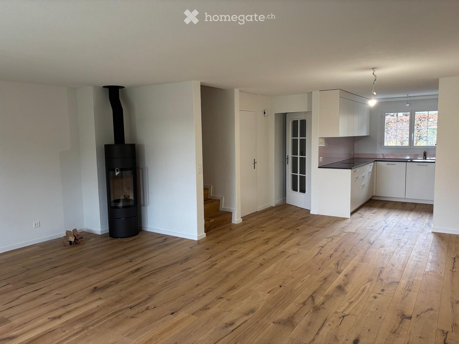 Open living space, fireplace, kitchen, stairs leading up, hardwood floors, windows
