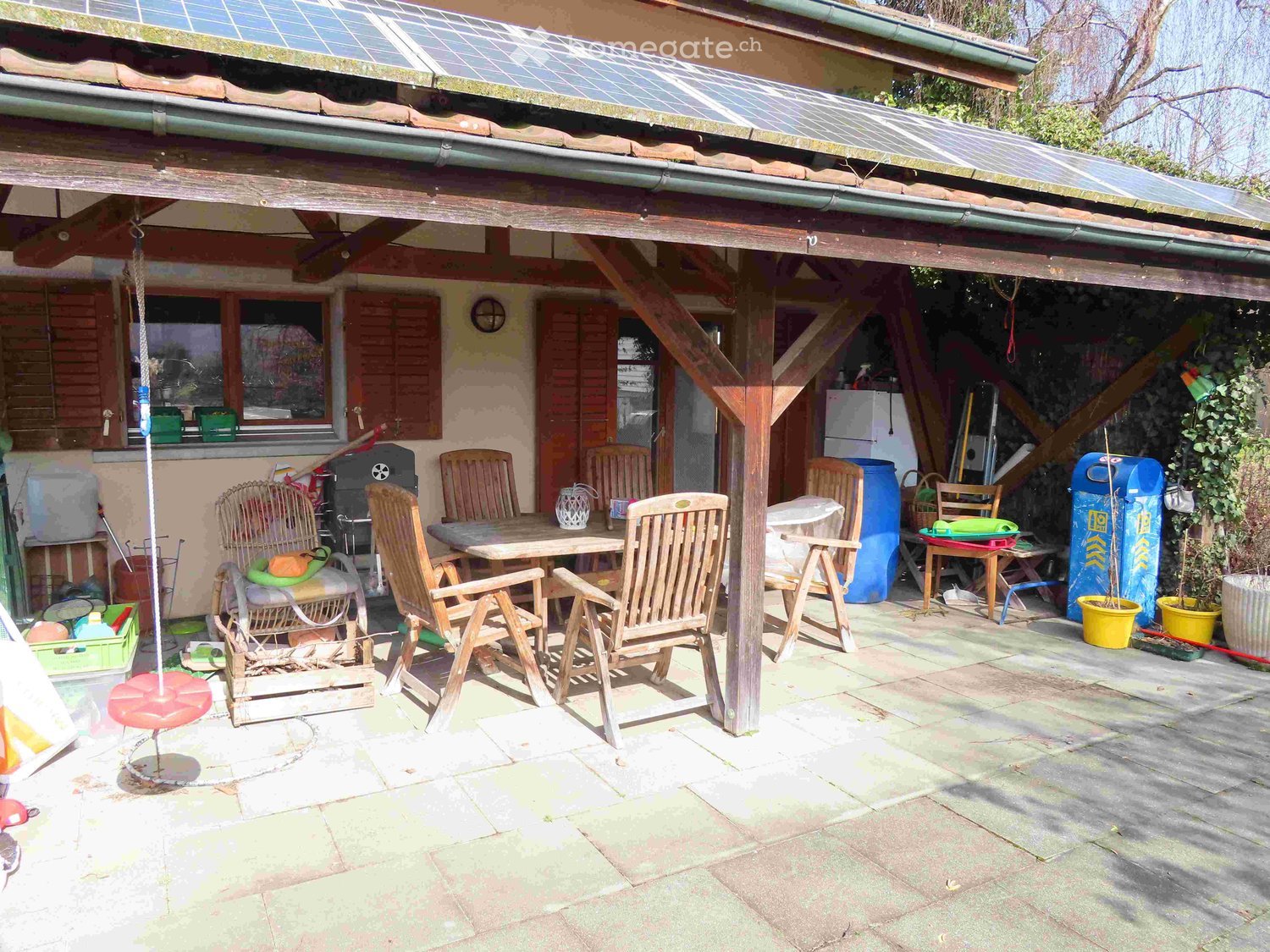 covered outdoor dining area with wooden table and chairs, solar panels on roof, storage boxes, and a swing