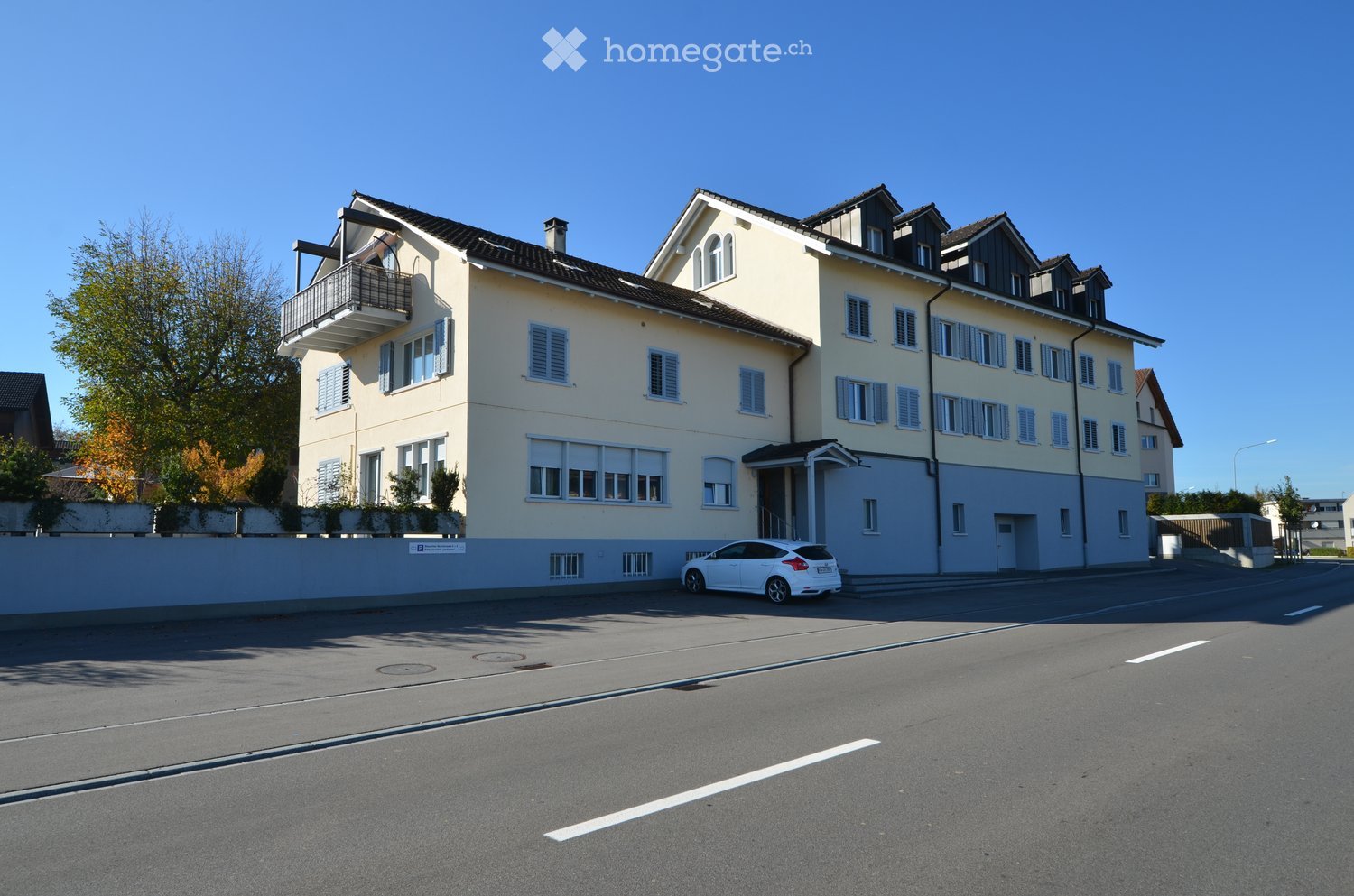 3 story building, balcony on the top floor, windows with shutters, parked car in front