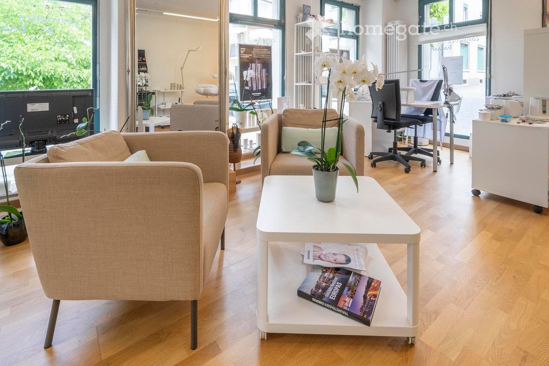 modern living room with beige couches, white coffee table, flower vase, magazines, wooden floor, large windows