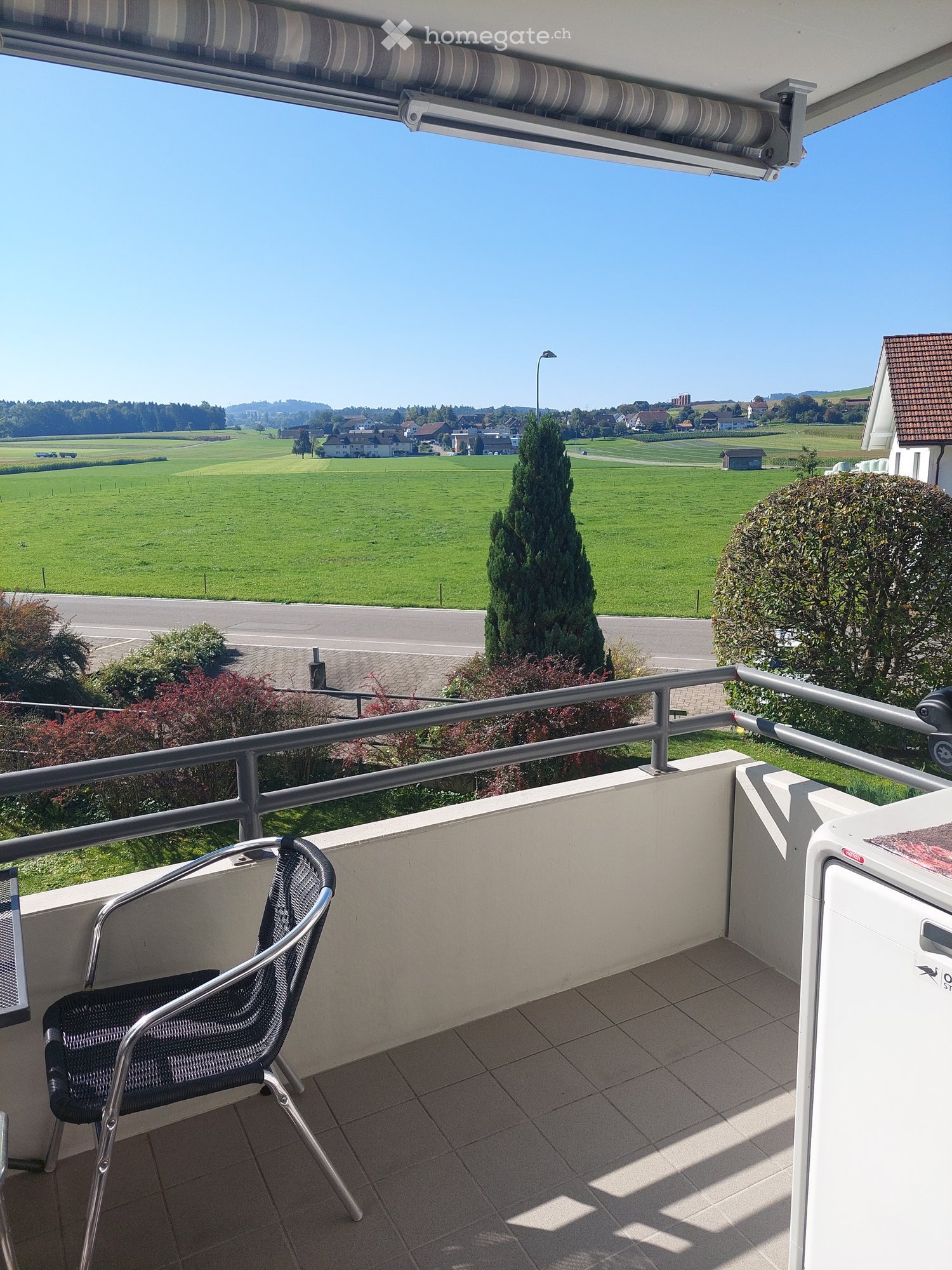 Balcony with metal railing, chair, table, tiled floor, view of a green field