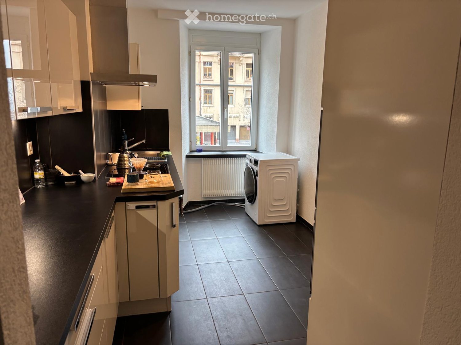 modern kitchen with black countertops, white cabinets, white washing machine, window with white radiator, tiled floor