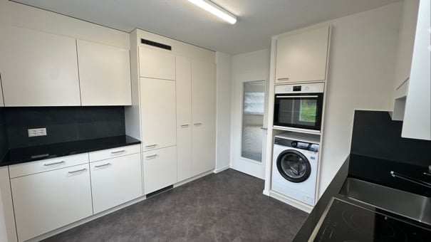 modern kitchen with white cabinets, black countertops, washing machine, dishwasher, microwave, sink, and a window