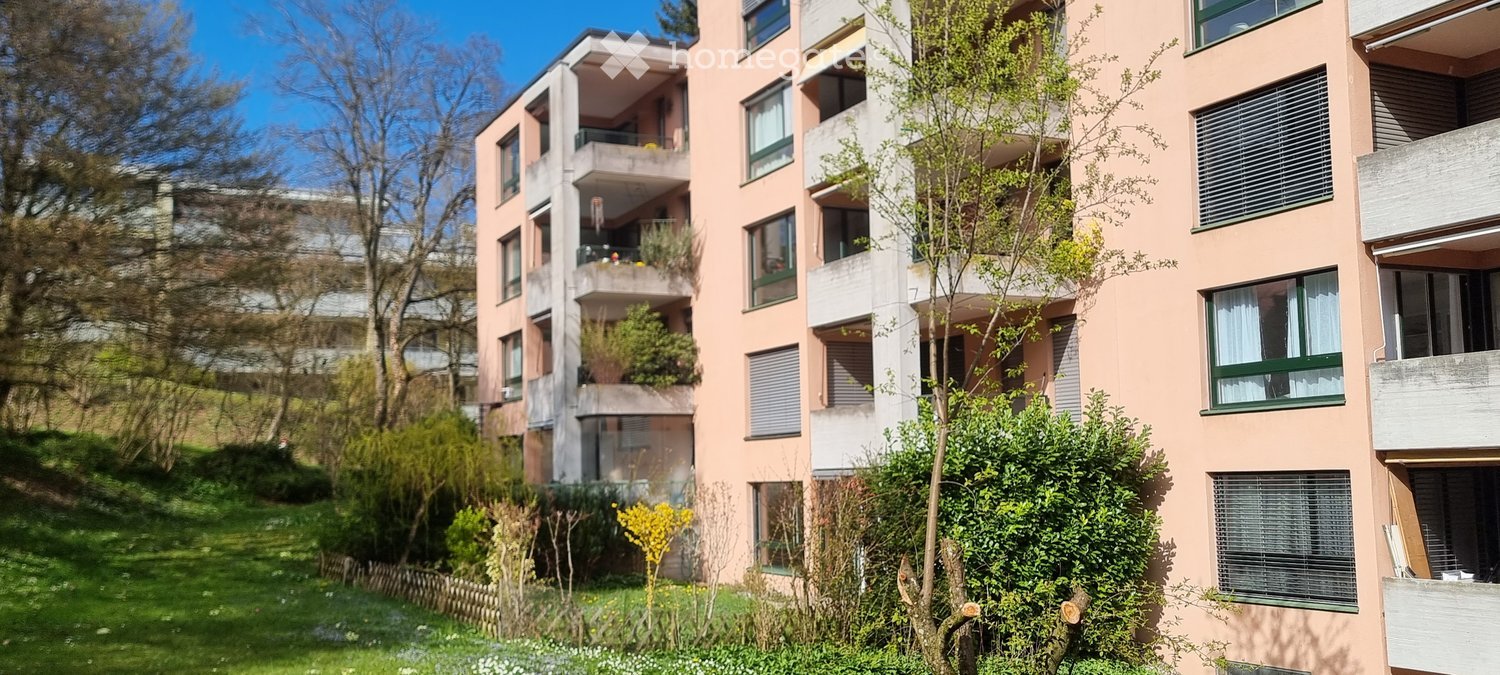 Apartment building with multiple balconies, pink exterior, multiple floors, greenery around