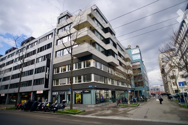 Modern multi-story building with glass windows, balconies, and a ground floor with shops