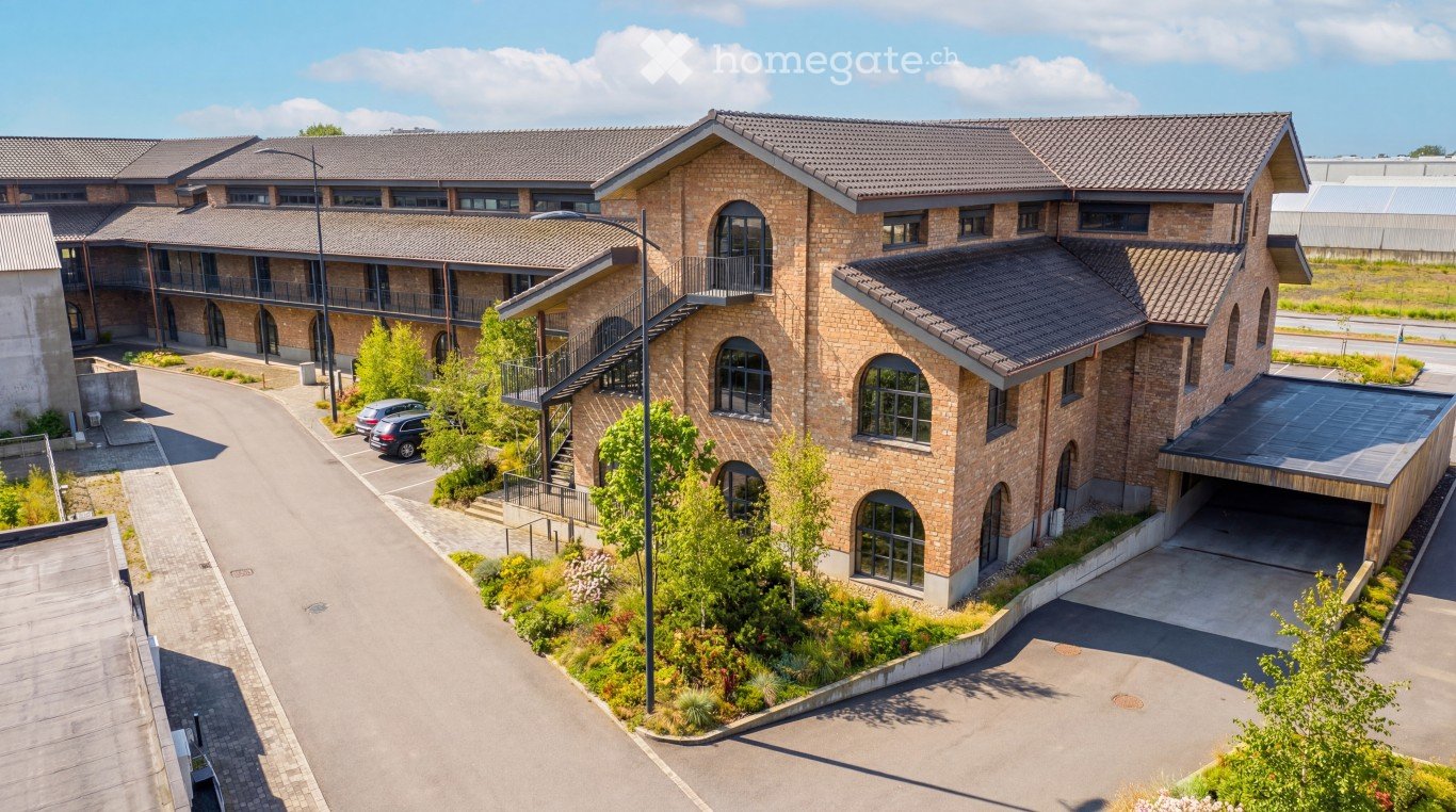 A large brick building with multiple floors, a driveway, and a parking area with cars parked in front.