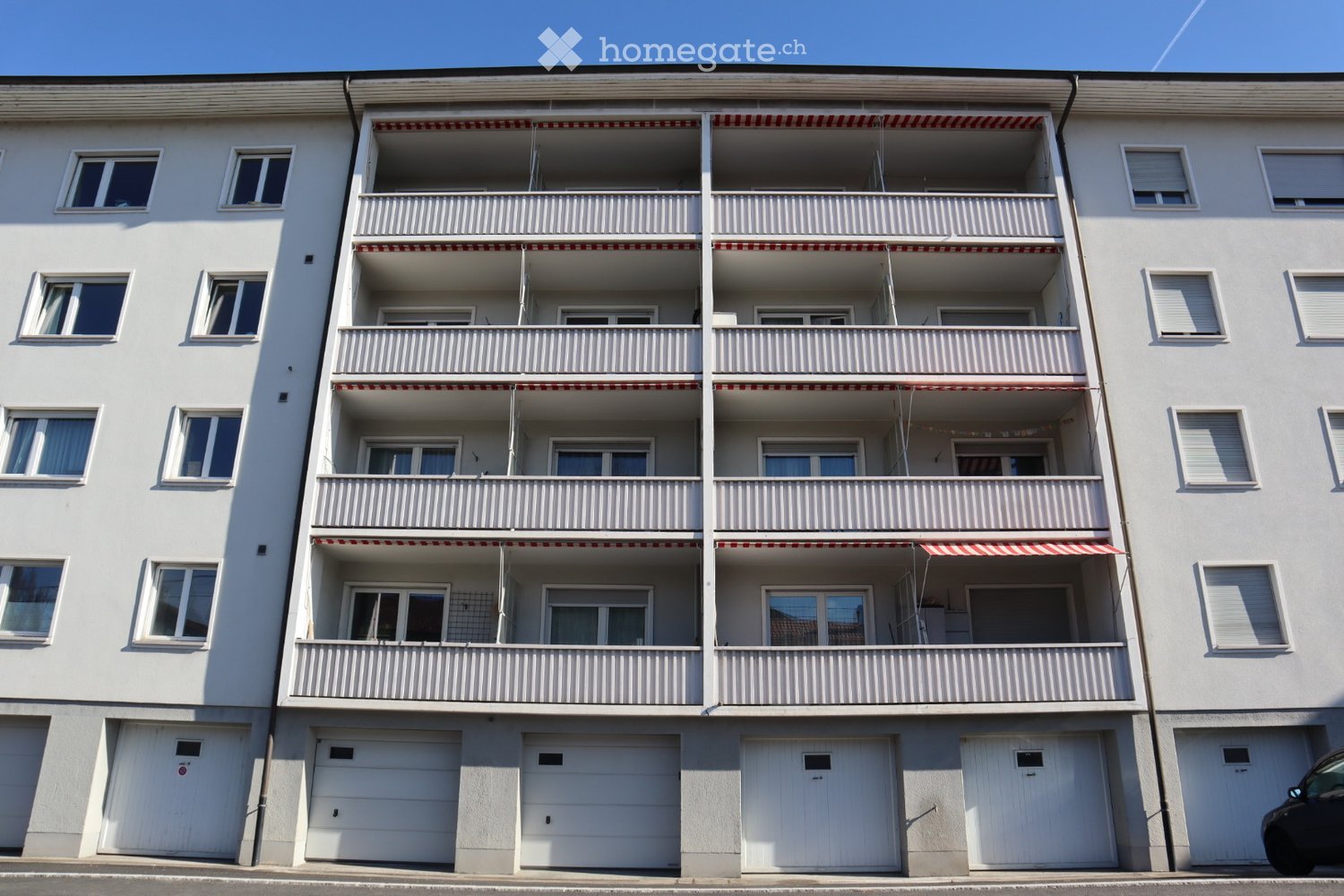 4 story apartment building, white exterior, multiple balconies, multiple garages