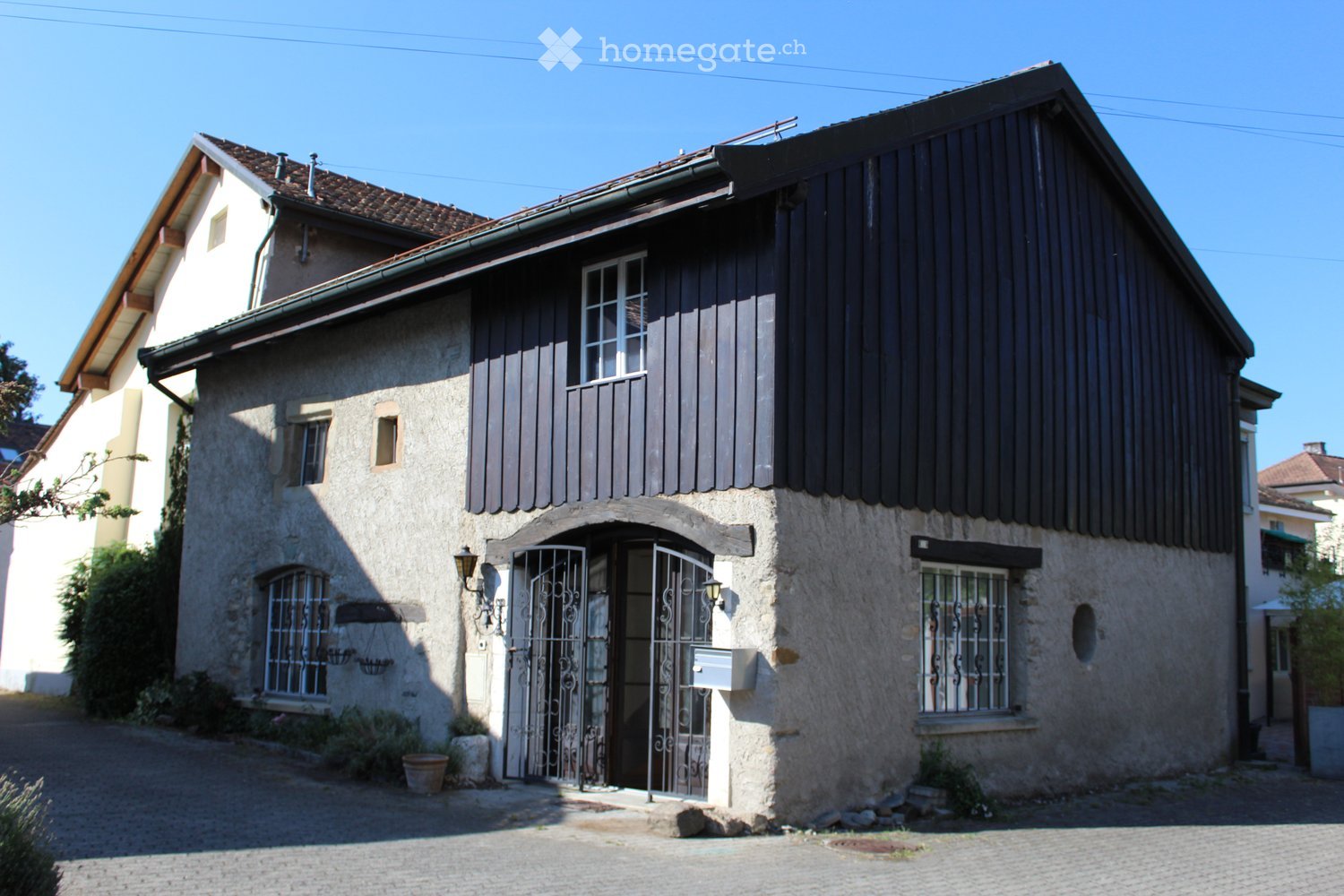 Stone house, black wooden facade, arched entrance, windows, lamp