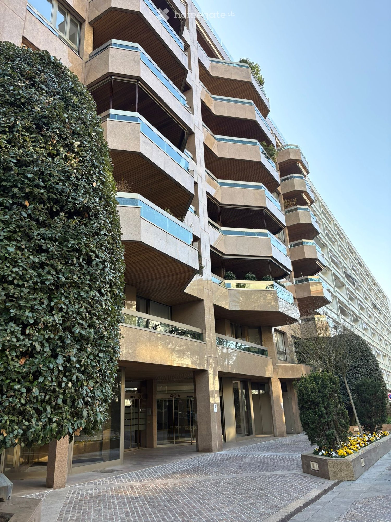 Modern apartment building with multiple balconies, glass windows, and a paved entrance.