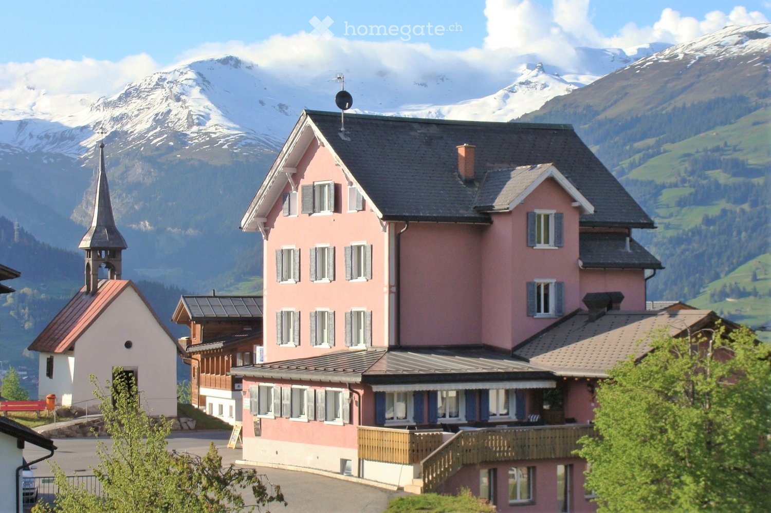 pink house, black roof, many windows, small church in the background, mountains in the background