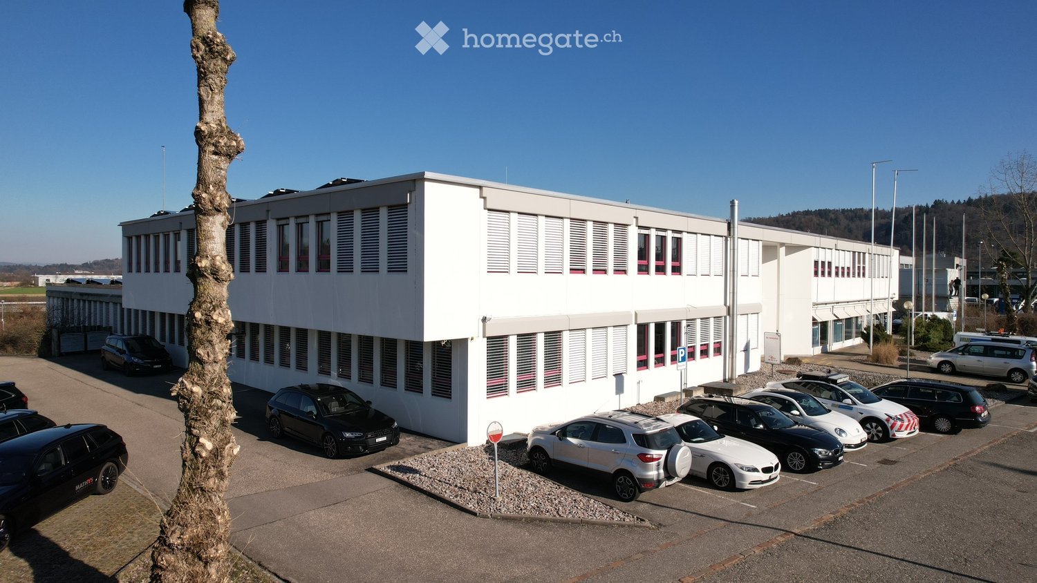 modern office building, white exterior, multiple windows, parking lot with several cars