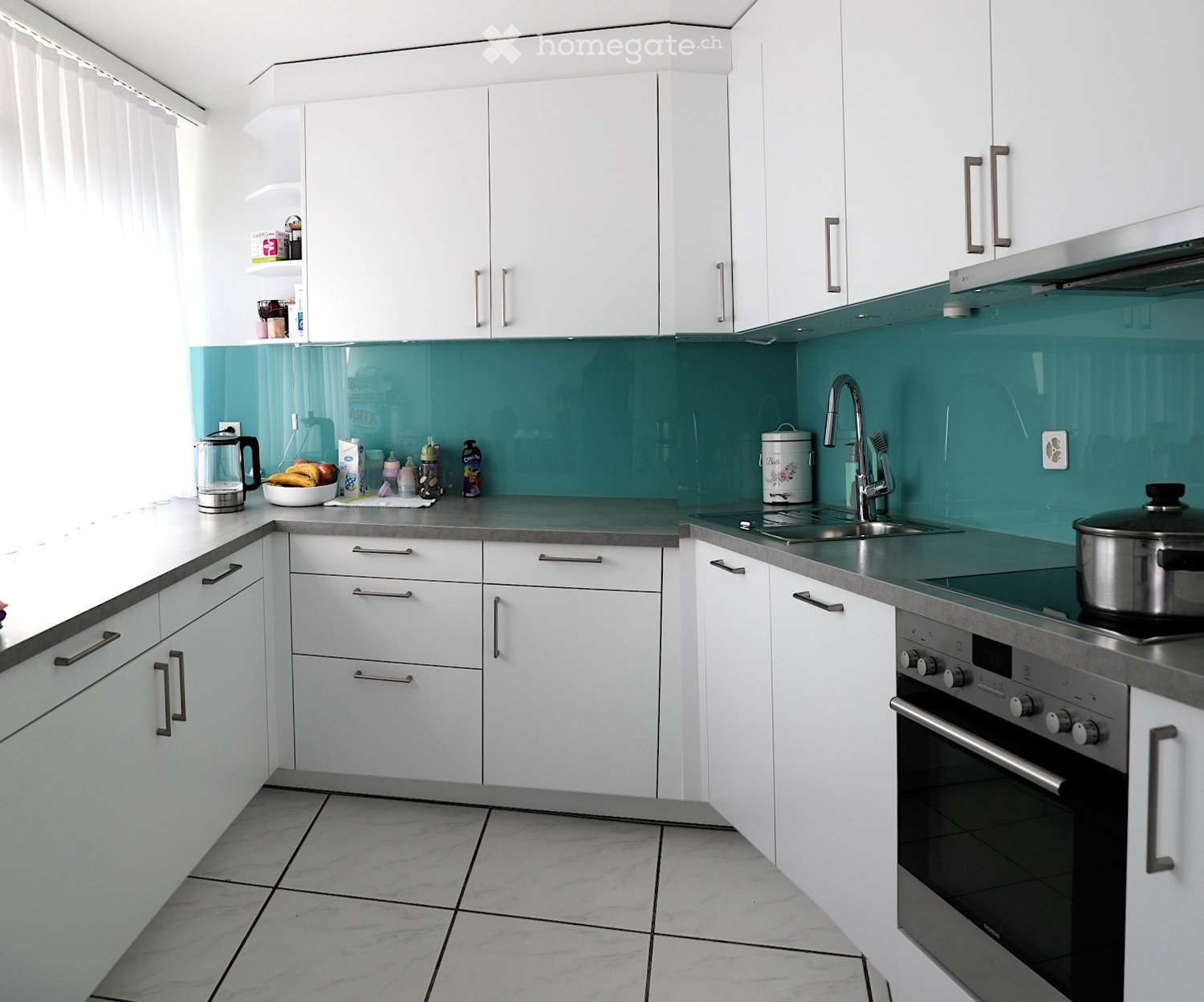 modern kitchen with white cabinets, teal backsplash, granite countertops, stainless steel appliances, white tiled floor