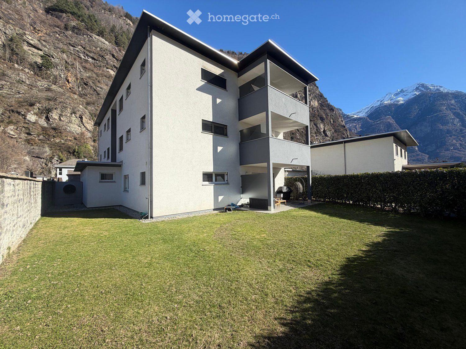 Modern white building with balconies, located in a mountainous area with a view of the mountains