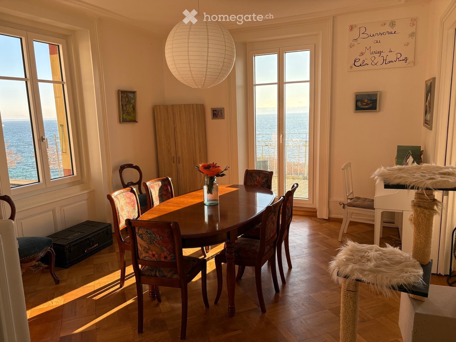 Dining room with wooden table, chairs, wooden cabinet, and large windows with sea view