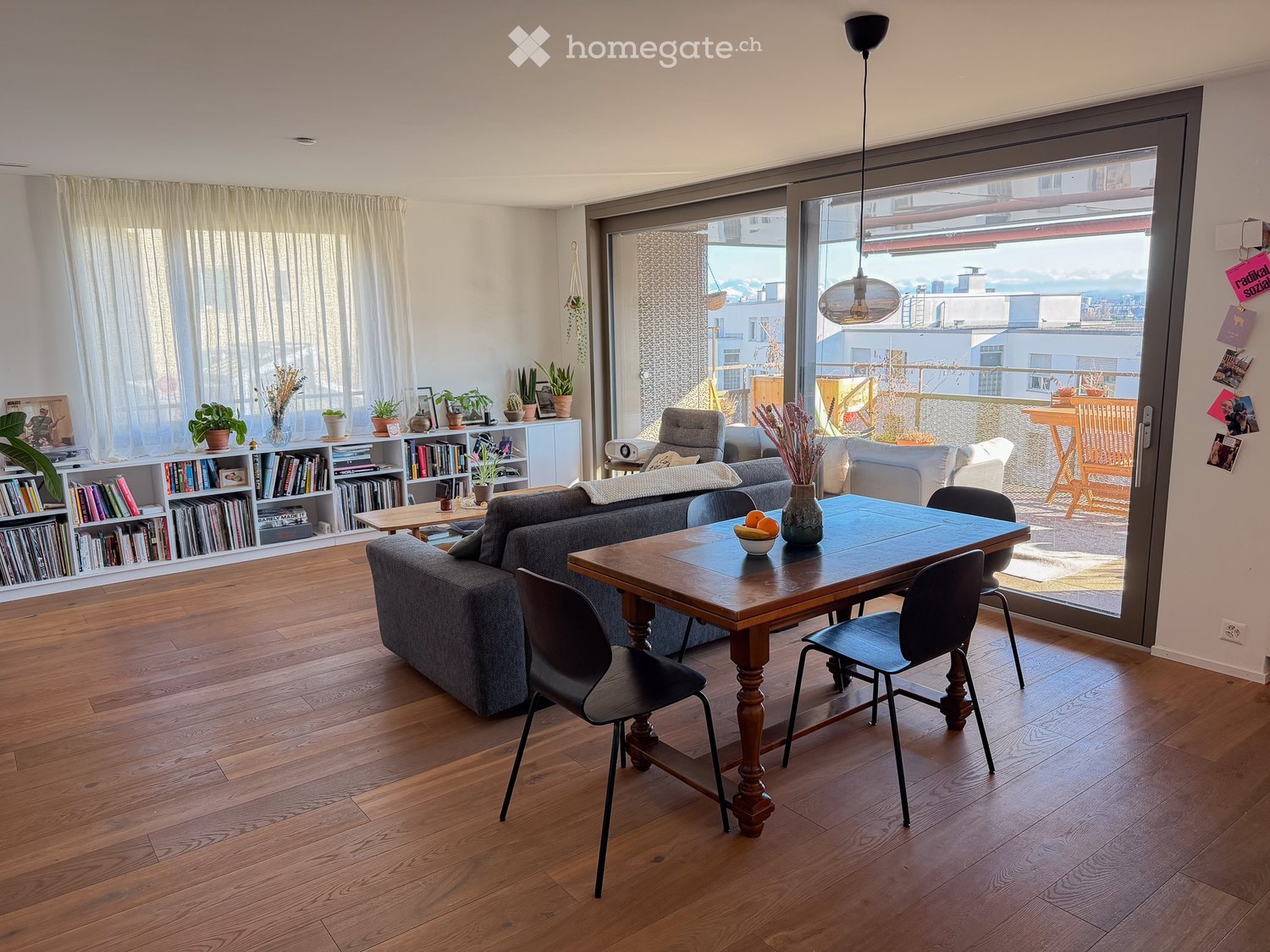 wooden floor, large windows, sliding glass door to balcony, dining table, couch, bookshelves, plants