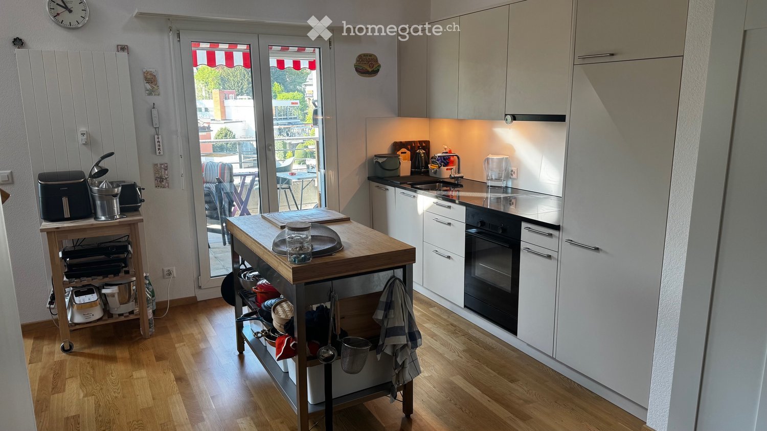 modern kitchen with white cabinets, wooden floor, large windows, balcony, view of the city
