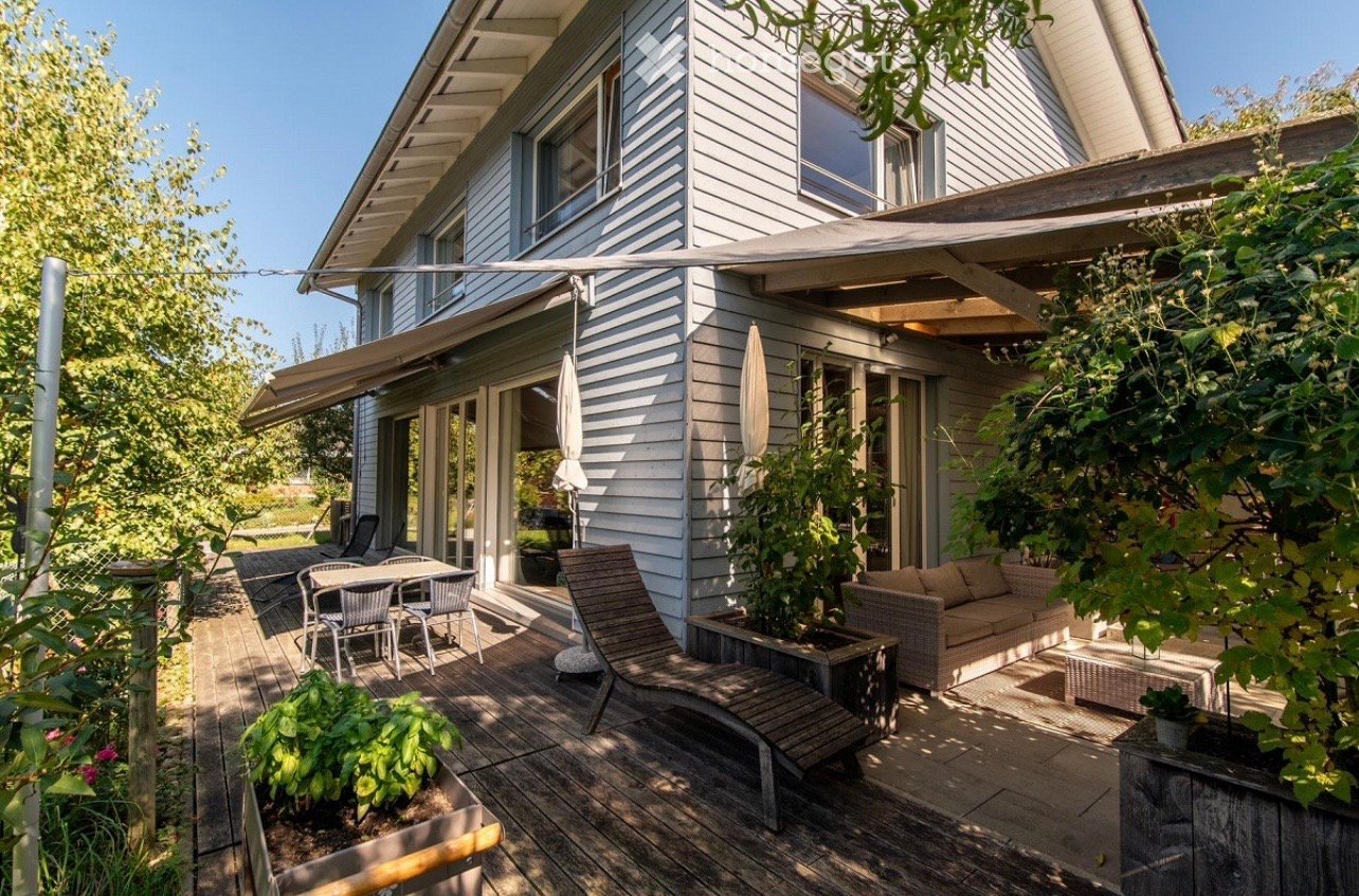 white wooden house, wooden deck, outdoor furniture, awning, plants, trees