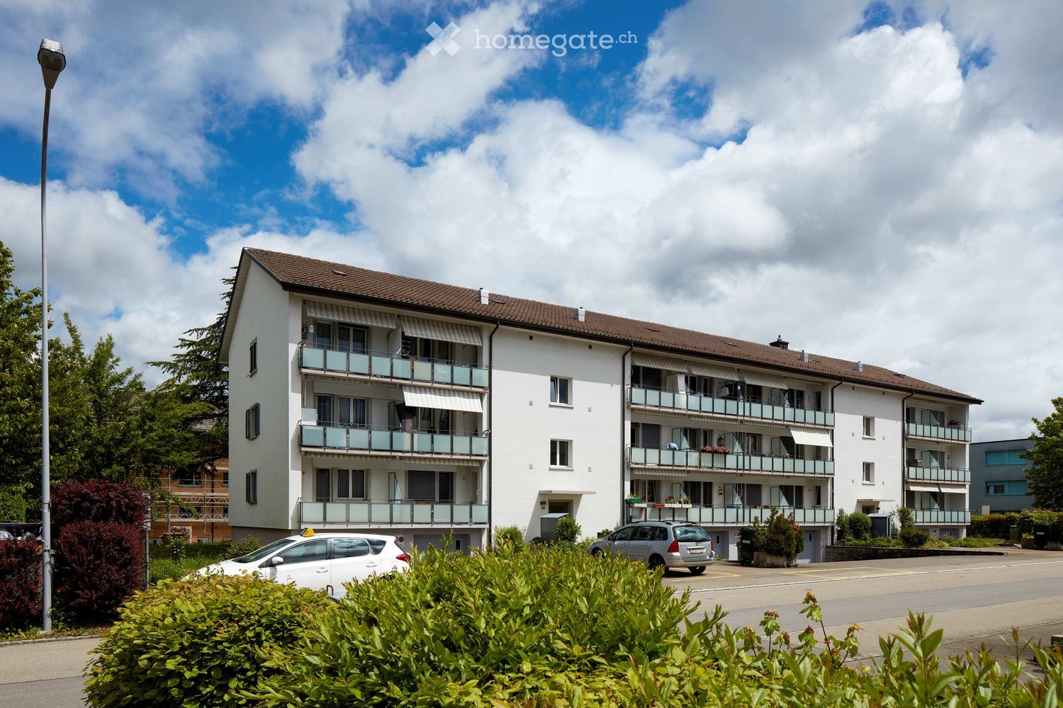 4 story apartment building, white exterior, brown roof, balconies, parking area