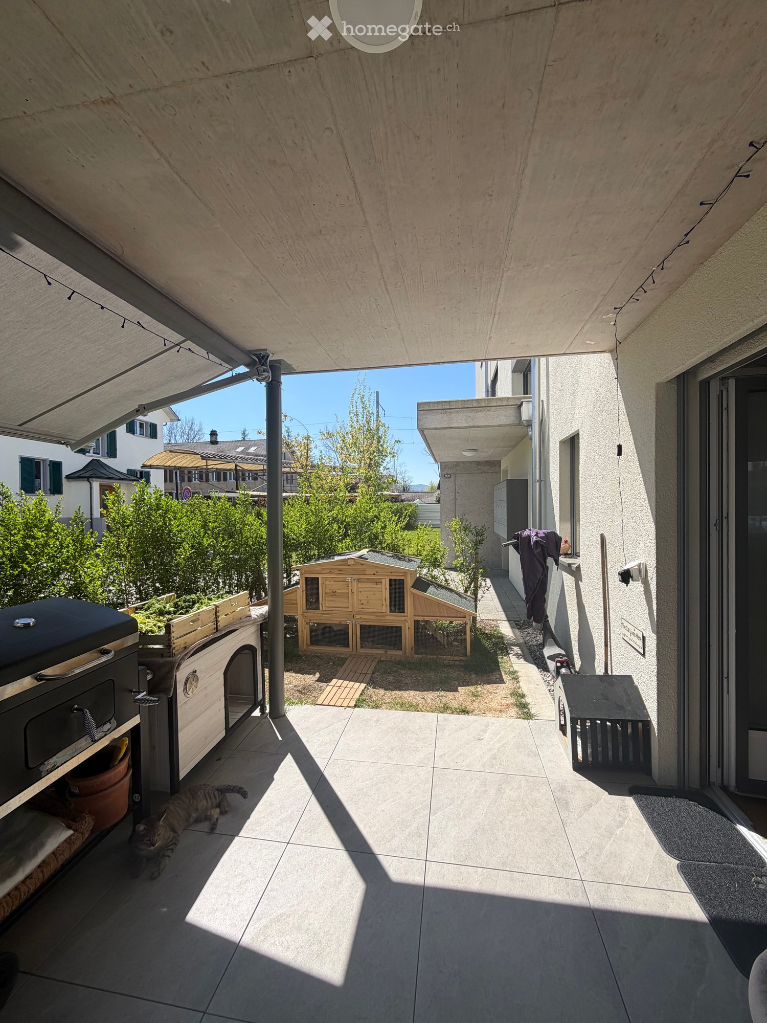 covered patio with tiled floor, outdoor grill, wooden chicken coop, potted plants, cat