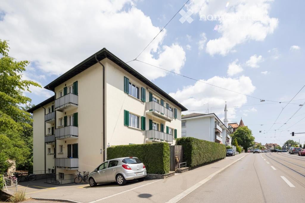 three story building, beige walls, green shutters, balconies, cars parked on street