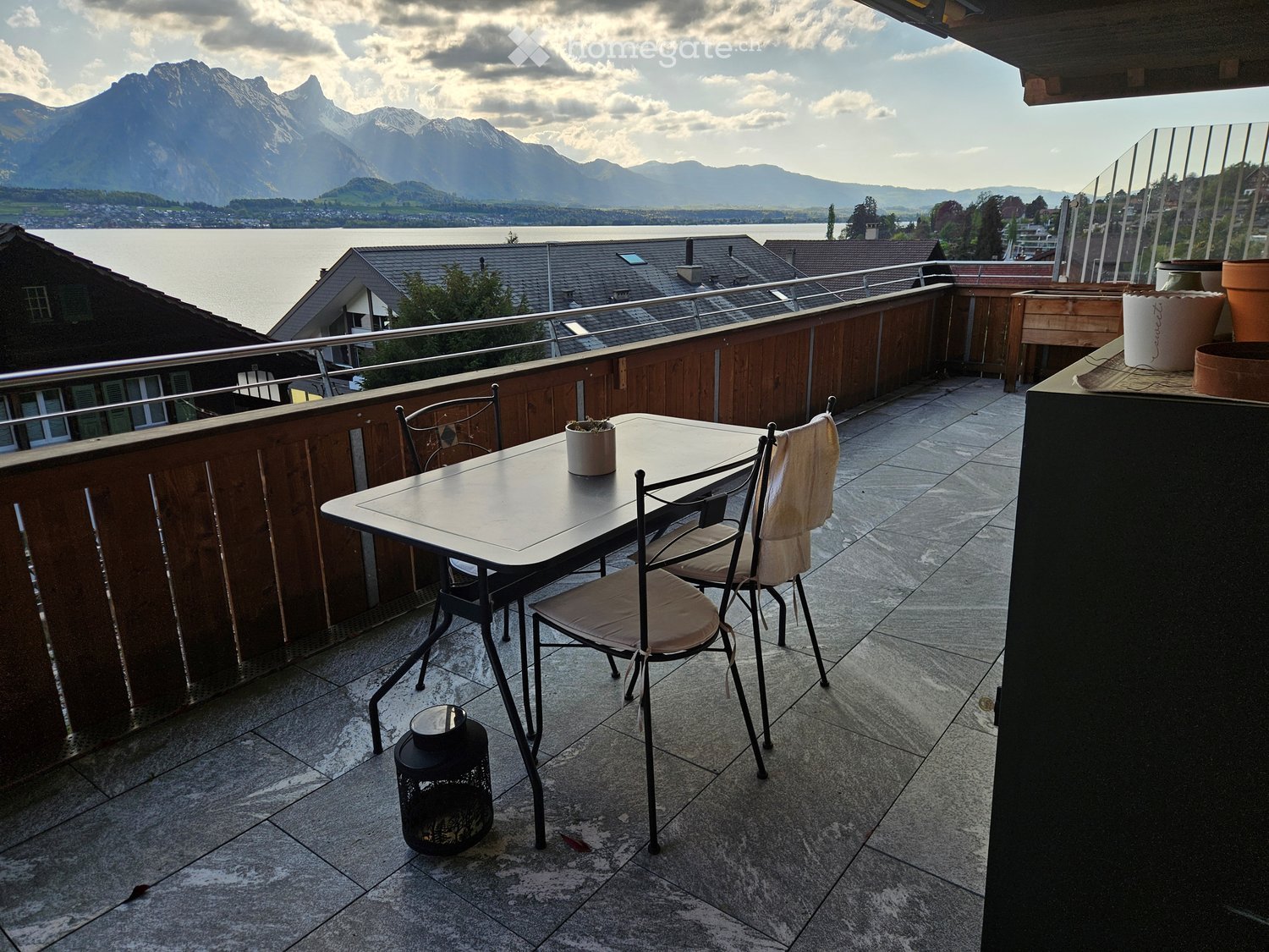 Balcony with table and chairs, wooden railing, lake view, mountains in the background