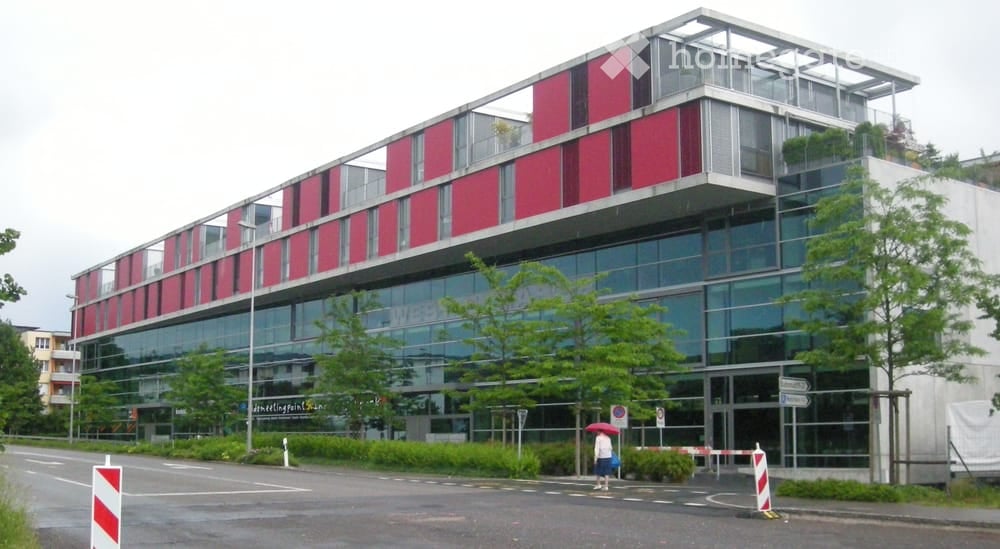 modern building, red and white exterior, glass windows, multiple floors, trees, street