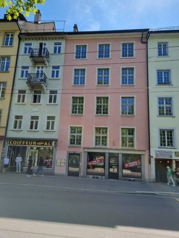A multi-story building with multiple windows and balconies, a shop on the ground floor, and people walking on the sidewalk.