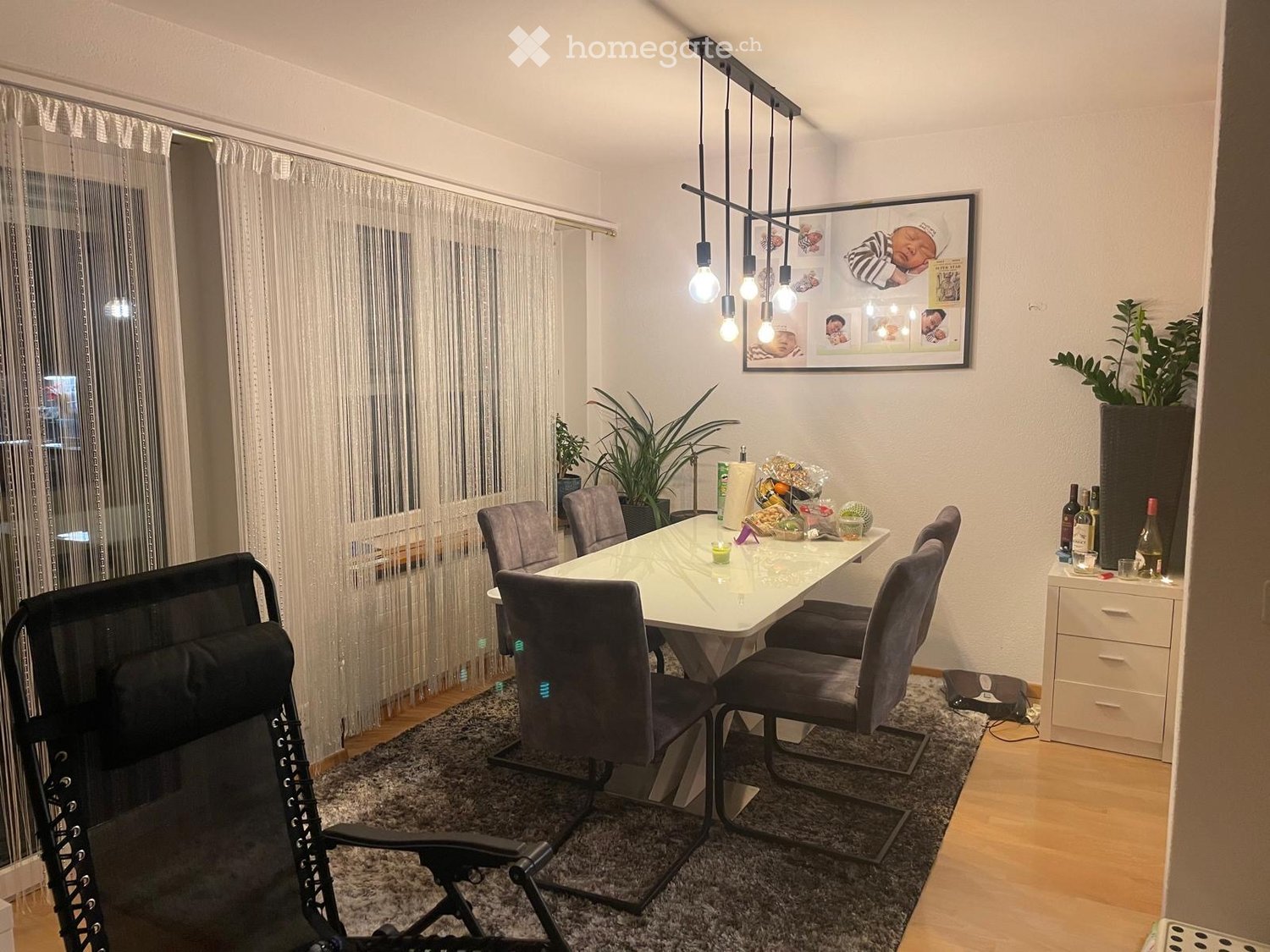 Dining room with a white table and chairs, a carpet, a white cabinet, a framed picture on the wall, and a chandelier with light bulbs.