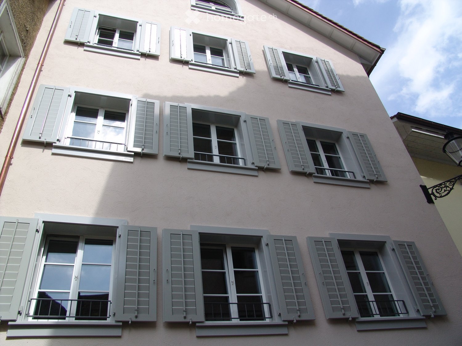 Facade of a building with multiple windows and shutters, pink wall, balcony on the top floor