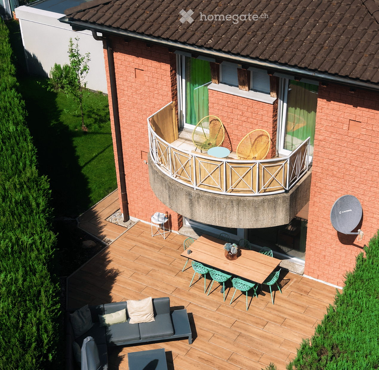 Wooden deck with a grey sofa, small table, and chairs. A round balcony with two yellow fans and a small table. Satellite dish on the wall.