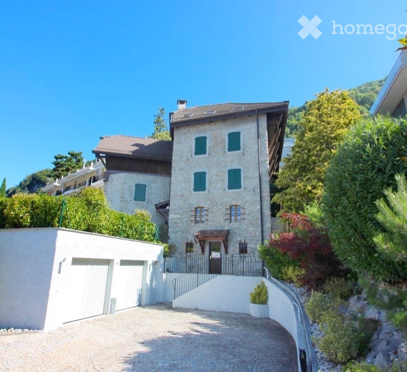 Stone house, 2 garages, driveway, garden, trees, mountain in the background