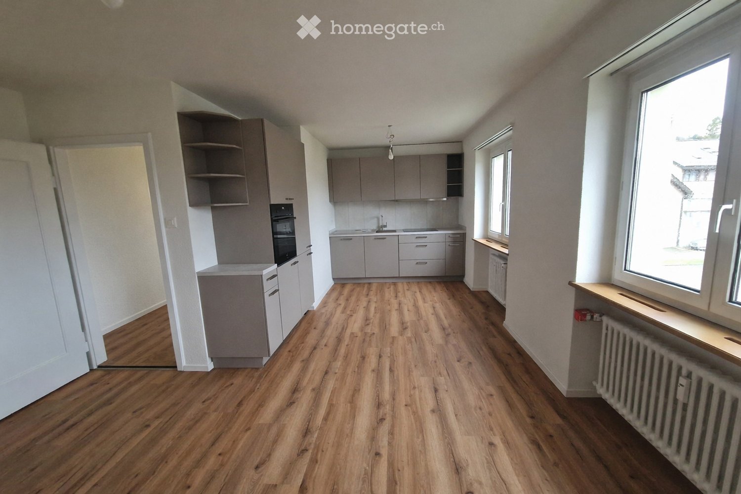 Empty kitchen with wooden floor, white walls, gray cabinets, built-in oven, sink, and windows