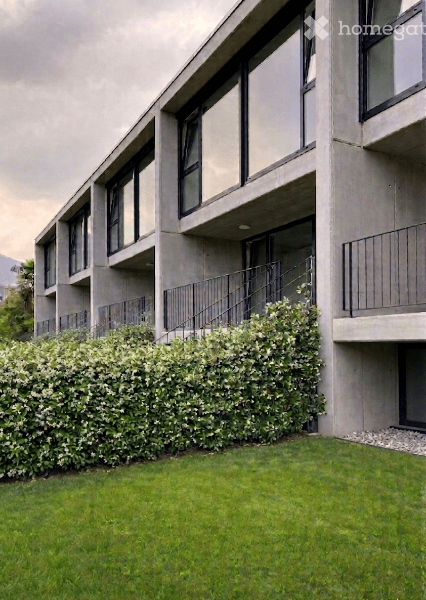 Modern apartment building, concrete exterior, large windows, multiple balconies, green lawn, hedge
