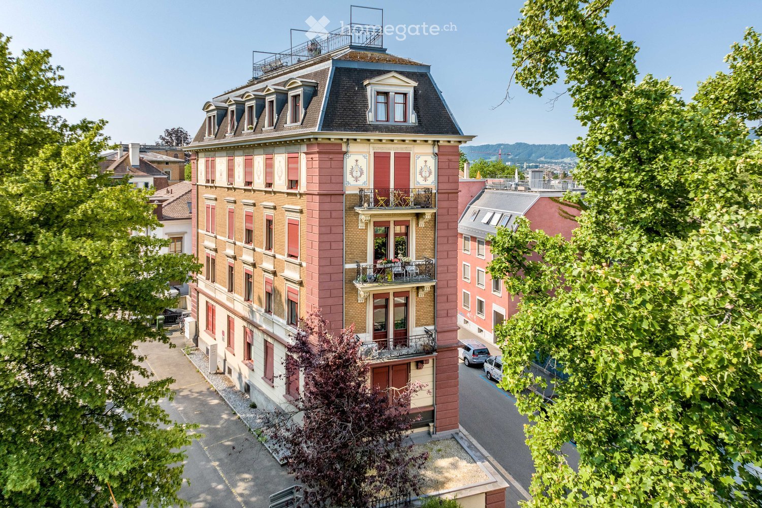 5 story building, red brick, white windows, balconies, trees, parking lot
