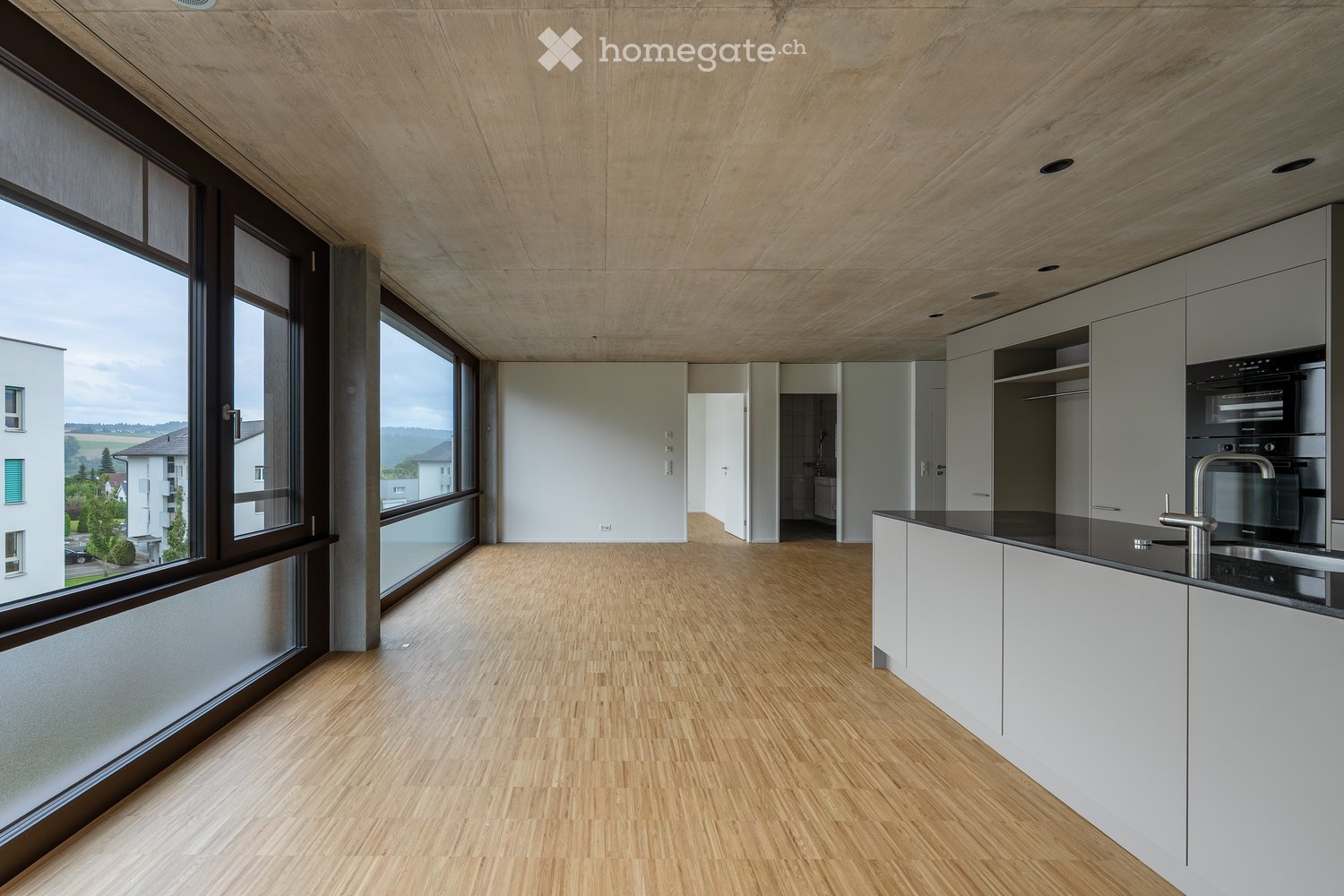 Modern kitchen with light wood flooring, white cabinets, black countertops, and large windows offering a view of the landscape.