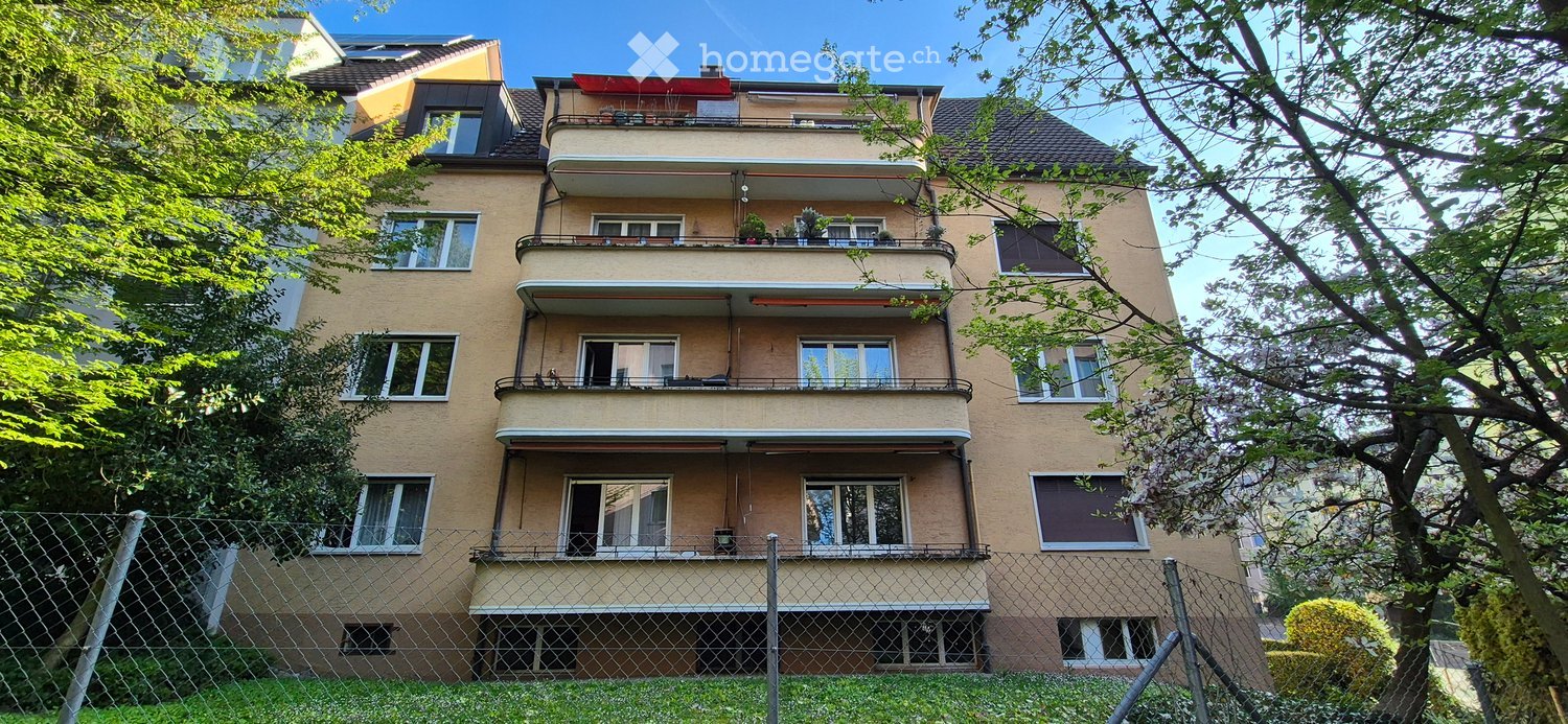 4 story building, beige exterior, multiple balconies, fenced yard, trees