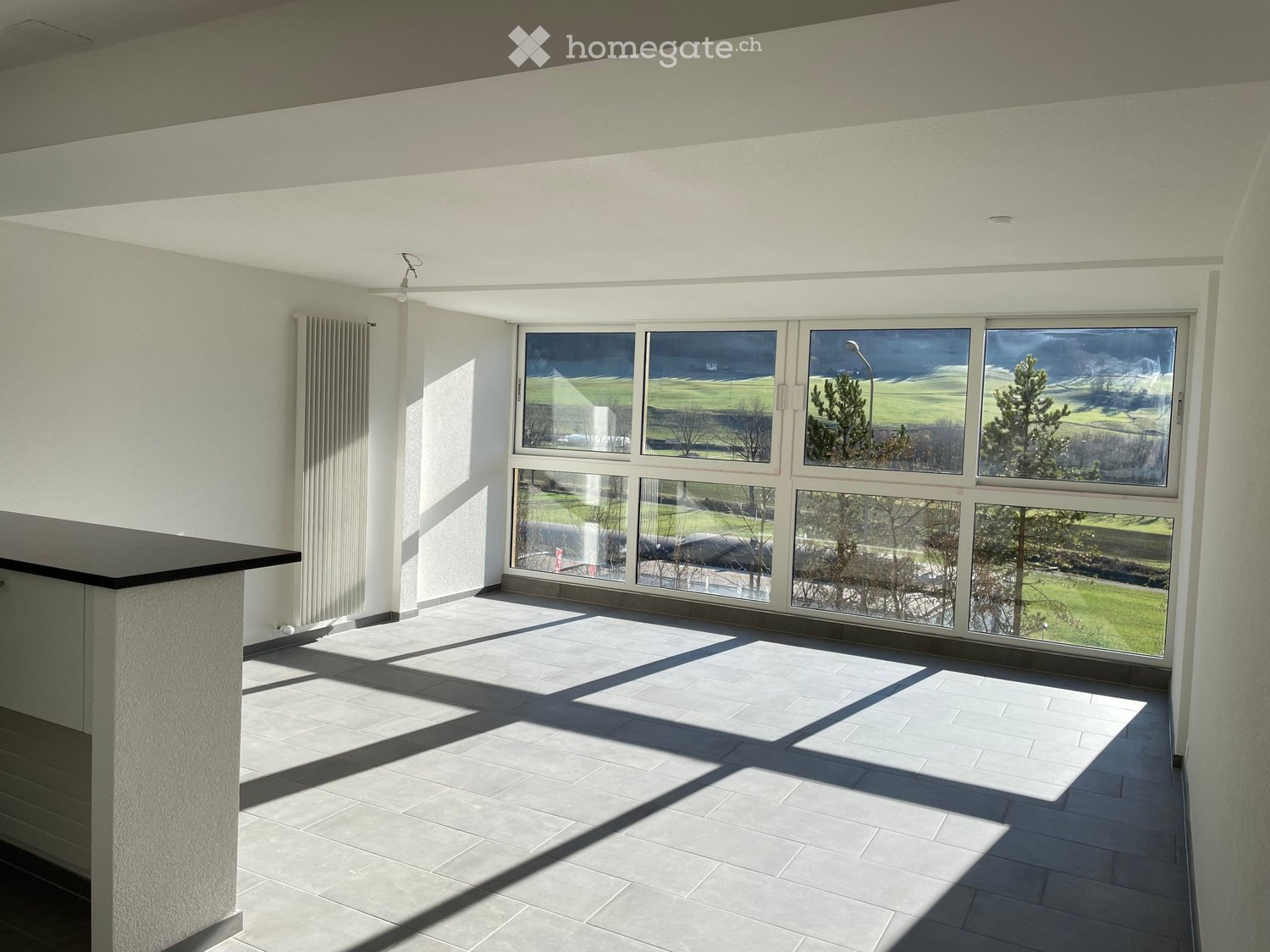 Empty room with large windows, tiled floor, white walls, and a view of a grassy field