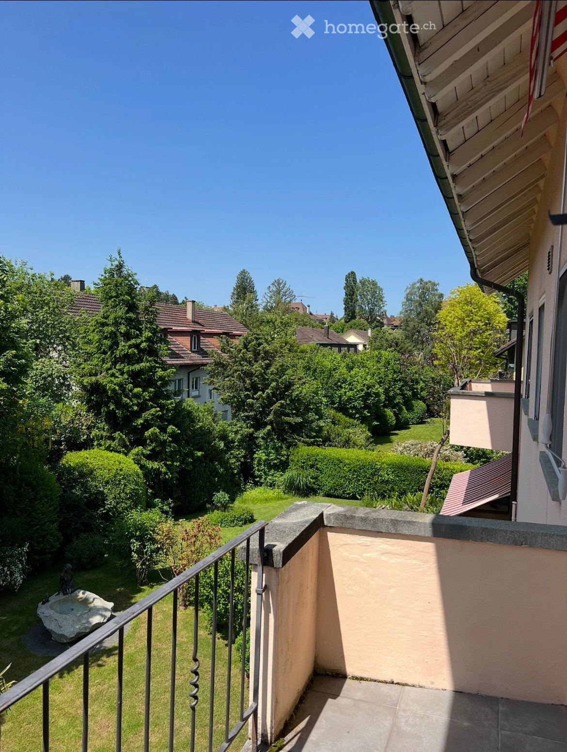 Balcony with metal railing, concrete floor, view of a garden and trees
