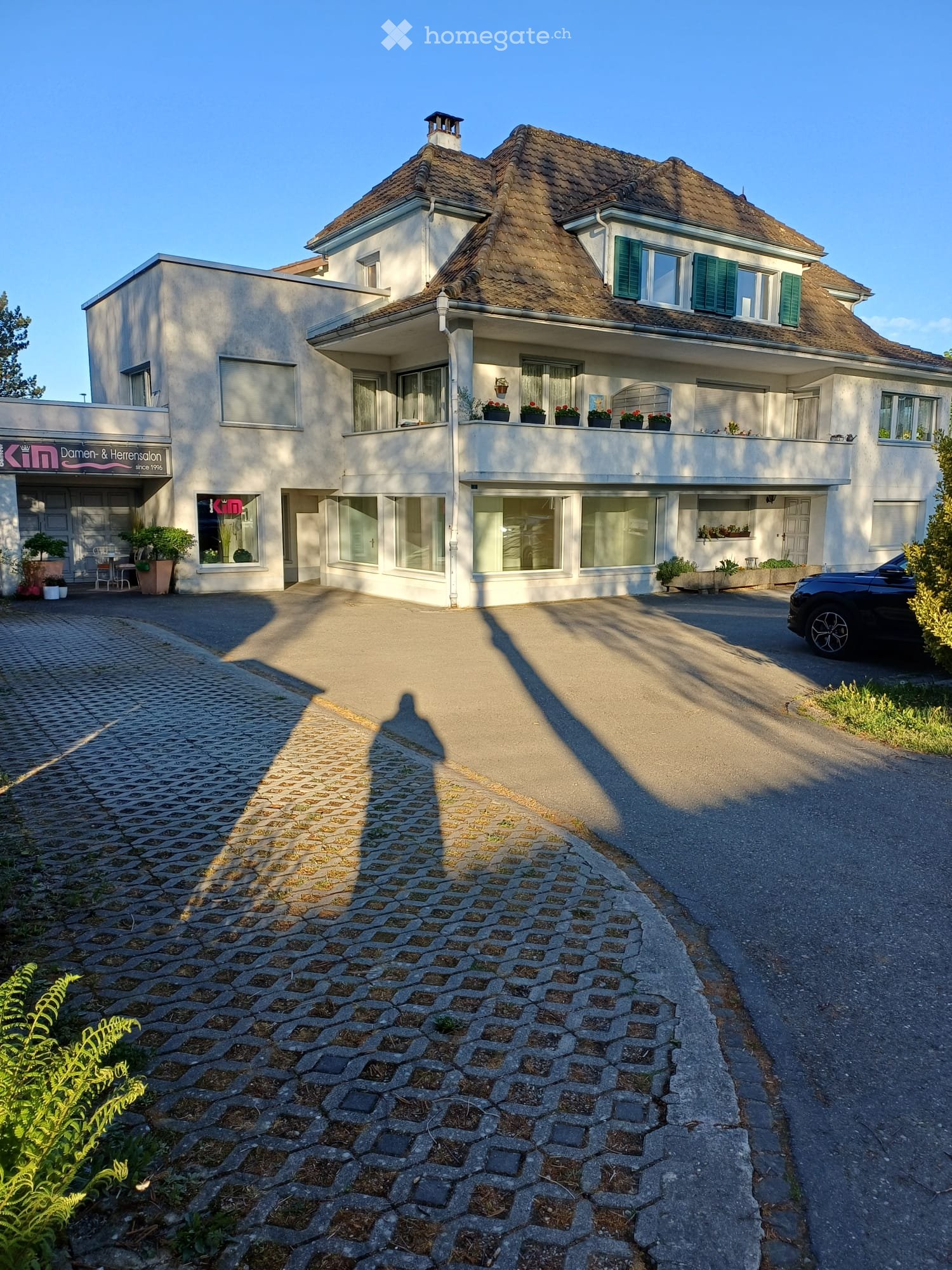 2 story house, brown roof, white walls, large windows, balcony with plants, car parked in front