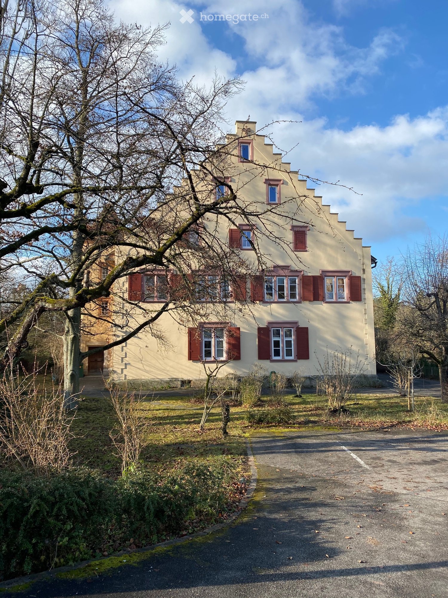 2 story house, beige walls, red shutters, large windows, driveway, trees, bushes