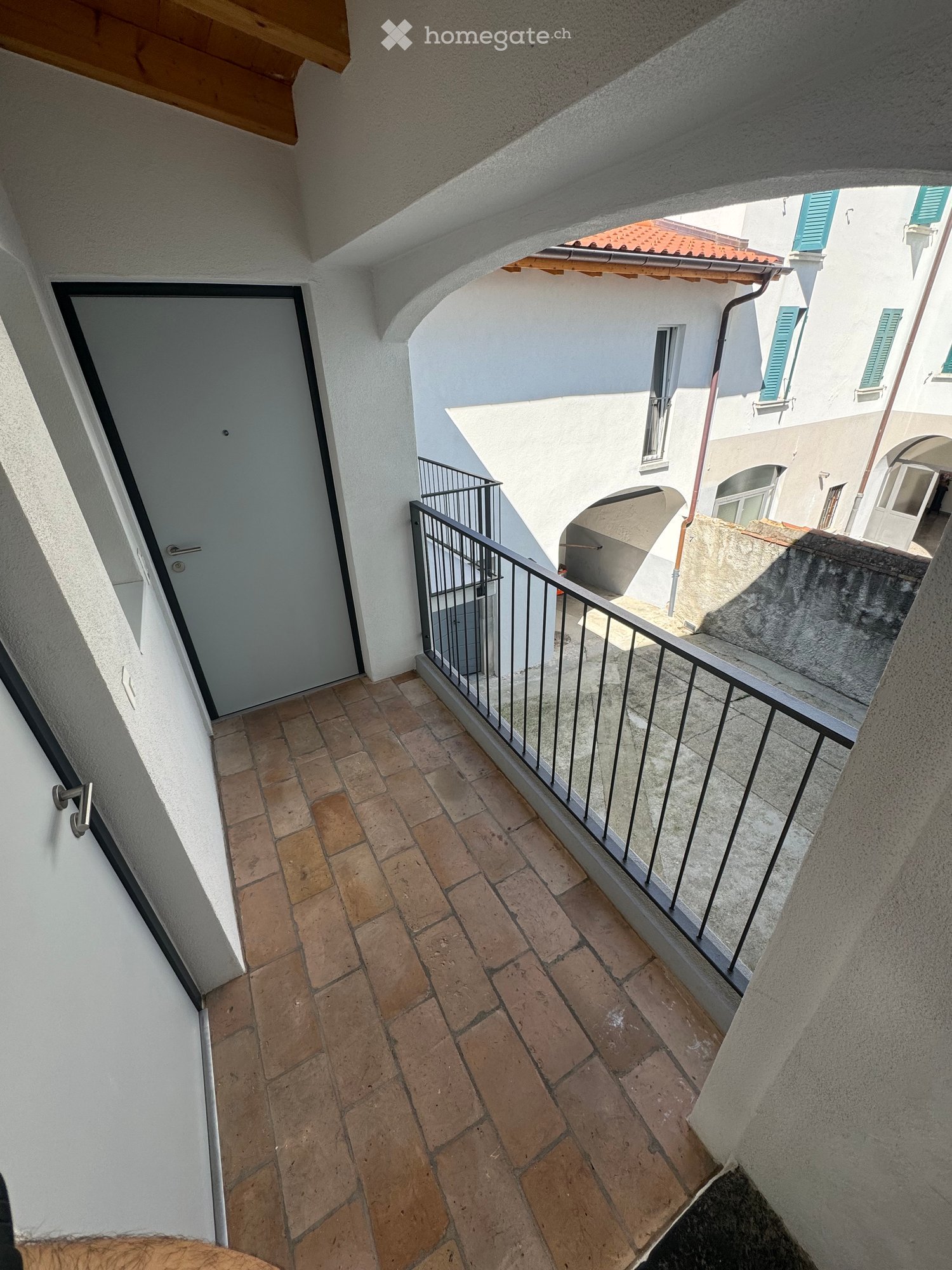 Balcony with brick floor, metal railing, white door, white walls
