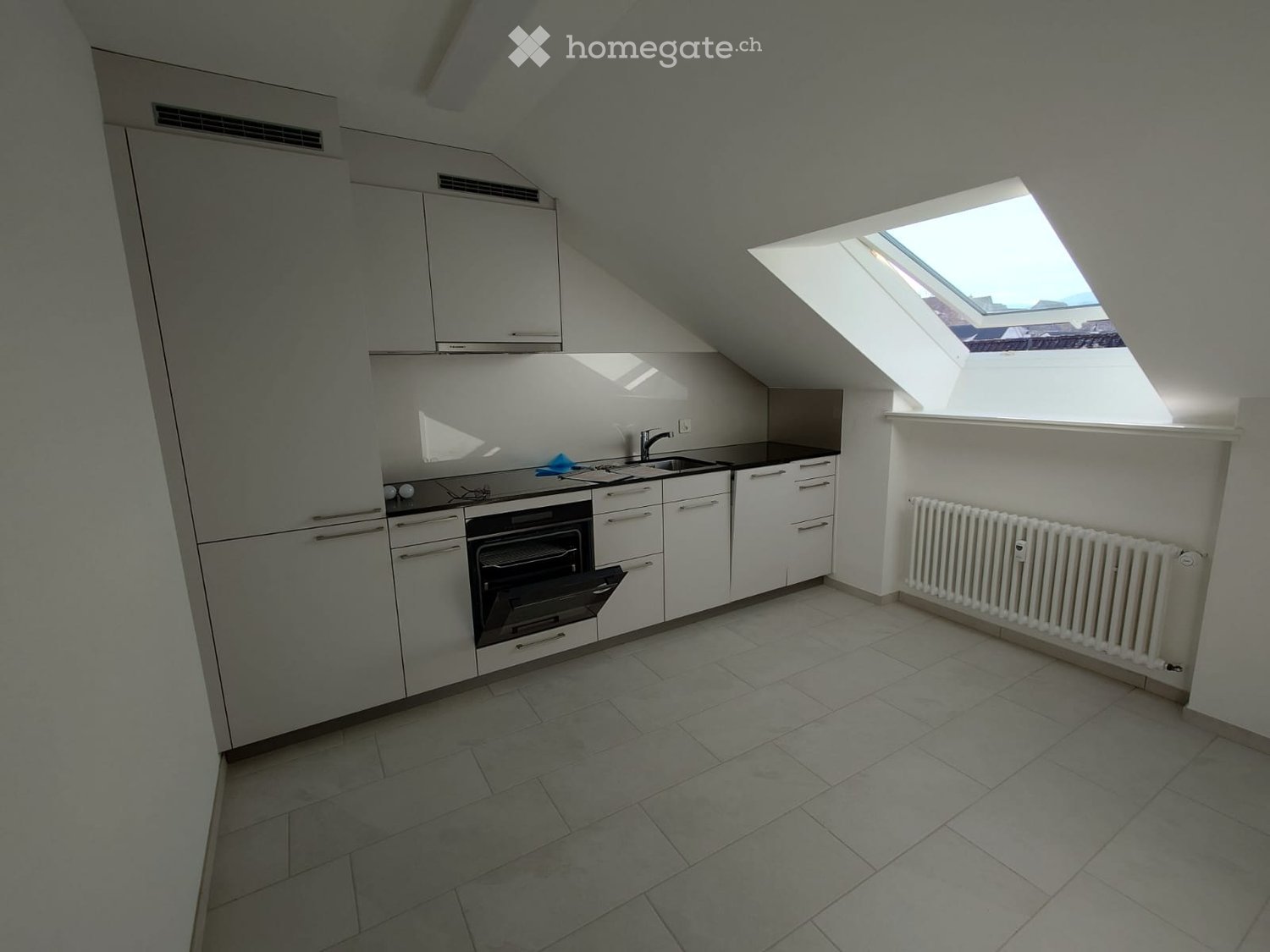 modern kitchen with white cabinets, tiled floor, black countertops, oven, sink, skylight