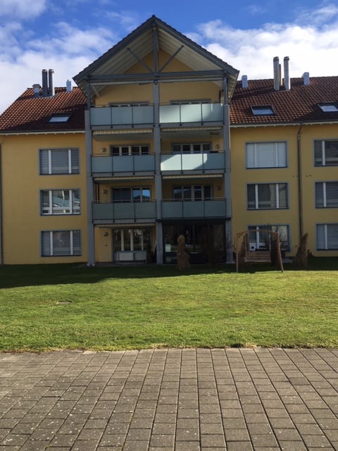 3 story yellow building, brown roof, many windows, balconies, large lawn in front