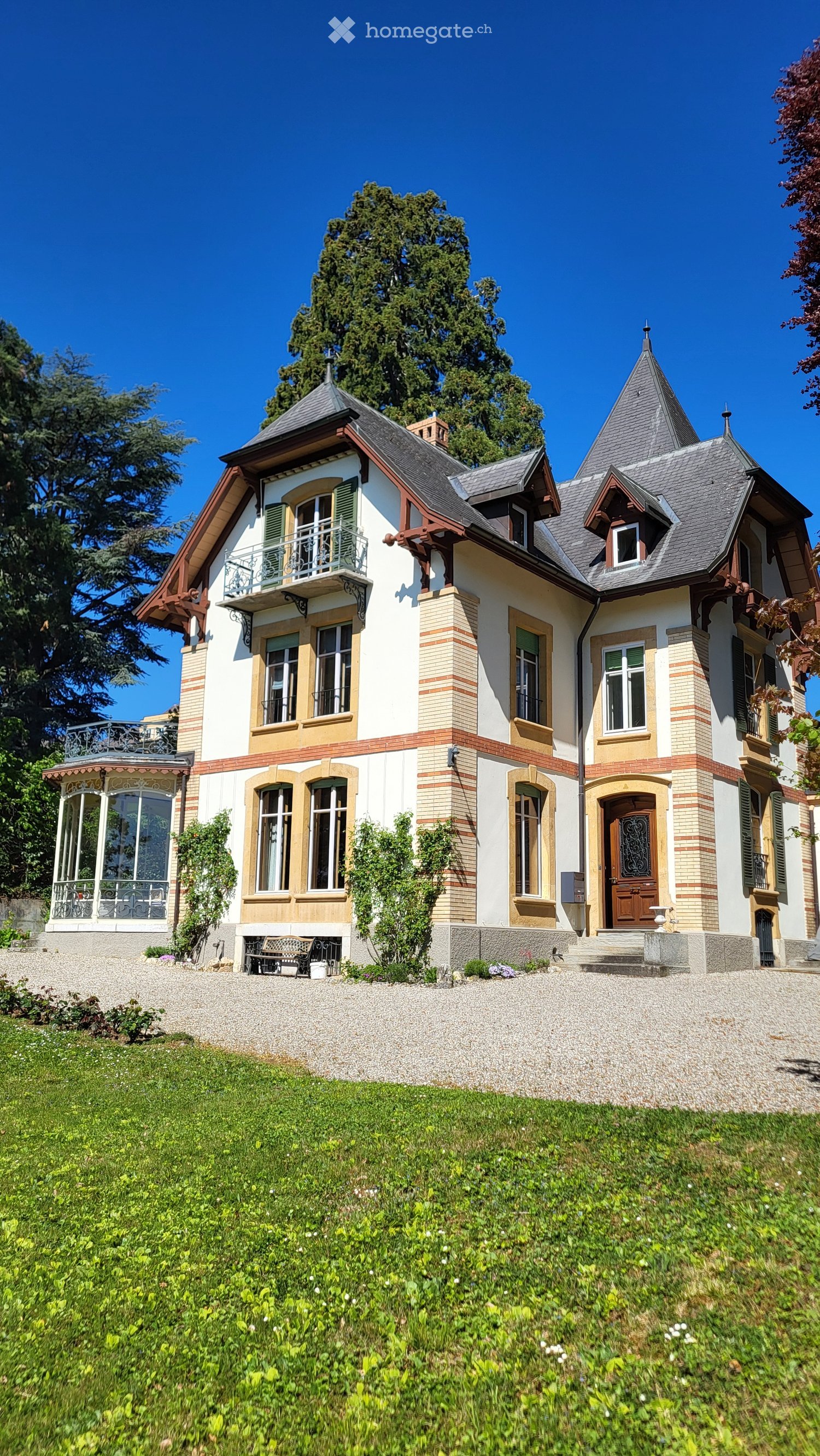 3 story house, white and brown exterior, large windows, balcony, gravel driveway, garden