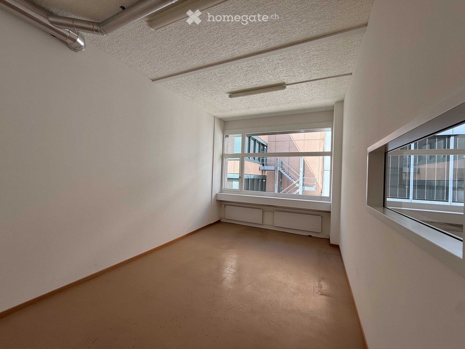 empty room, white walls, brown floor, large windows, view of building outside
