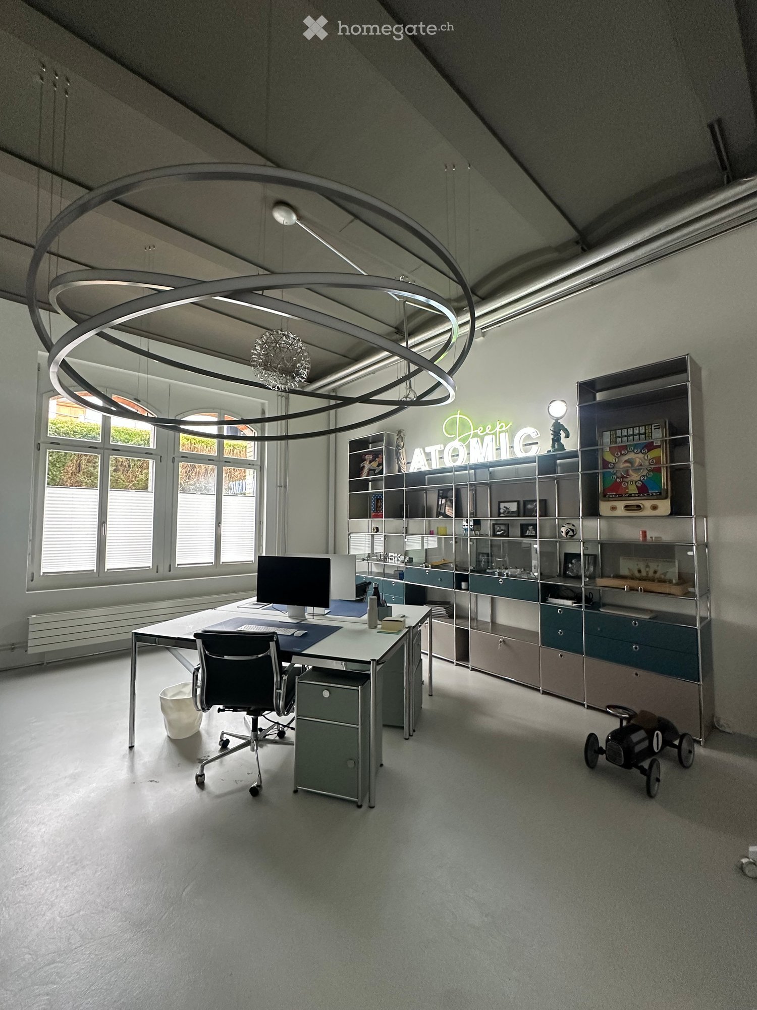 modern office with desk, chair, computer, shelves, toy car, circular ceiling lamp