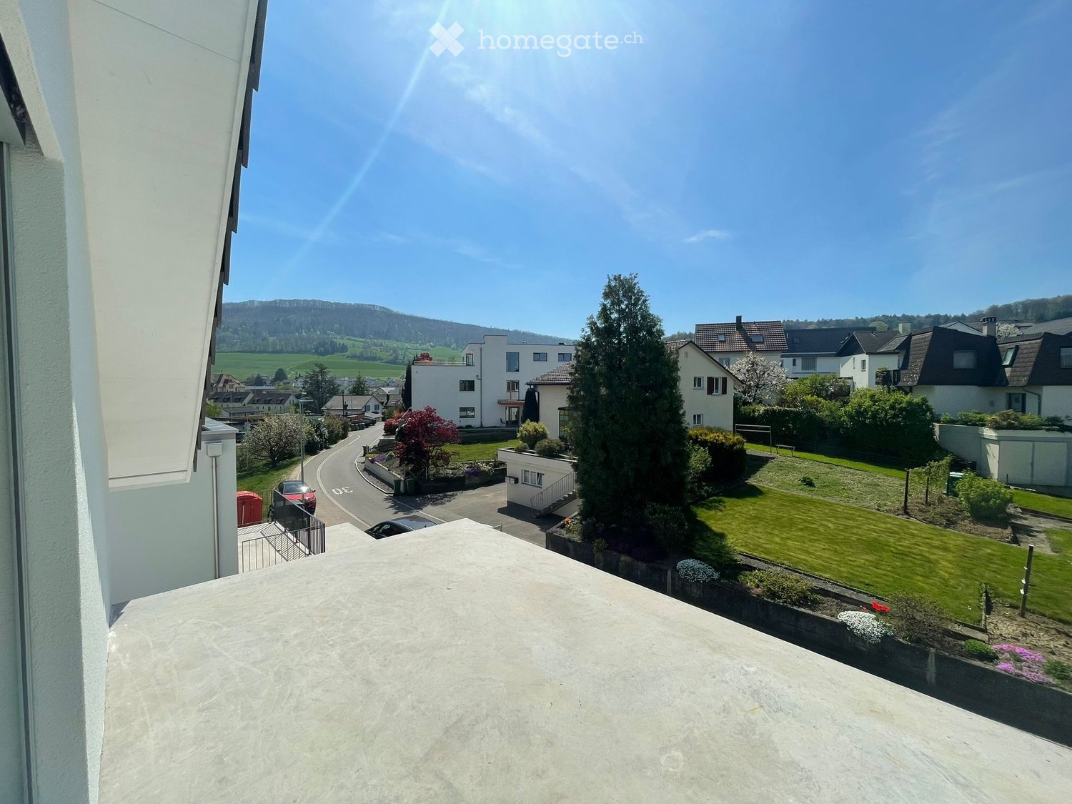 A balcony with a view of a neighborhood with houses, a road, and a green landscape.