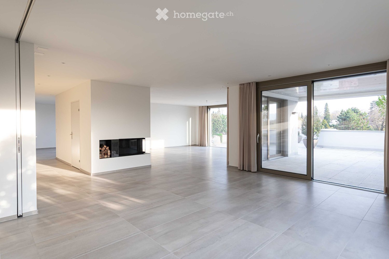 Spacious room with white walls, tiled floor, fireplace, and sliding glass doors.